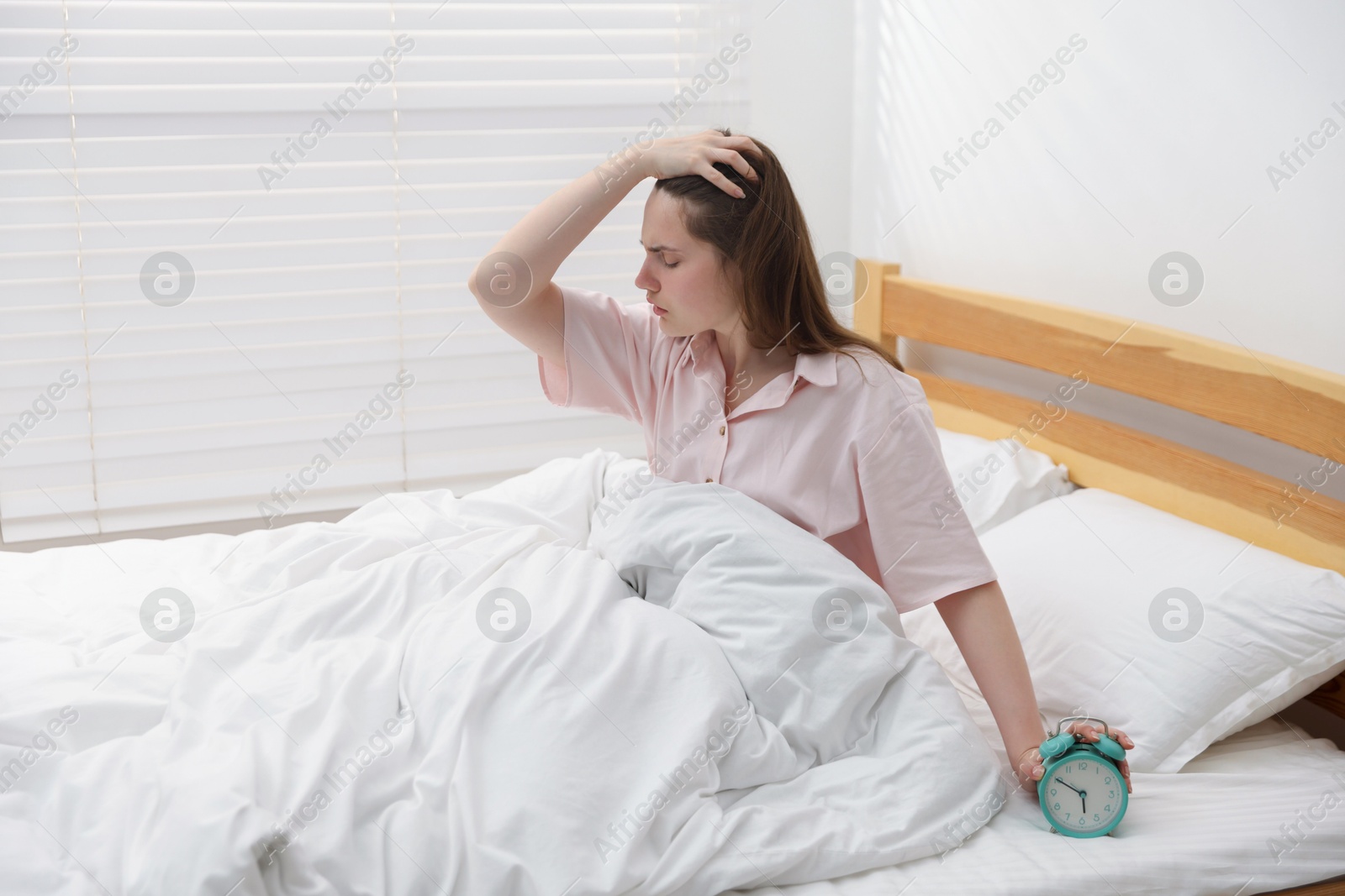 Frustrated young woman with alarm clock on bed at home Photo of Frustrated young woman with alarm clock on bed at home