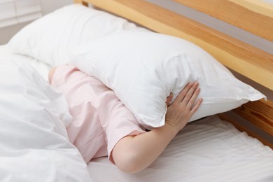 Photo of Woman covering herself with pillow on bed at home. Insomnia problem