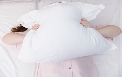 Photo of Woman covering herself with pillow on bed at home, above view. Insomnia problem