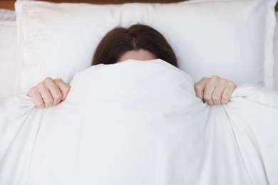 Photo of Woman covering herself with blanket on bed at home, above view. Insomnia problem