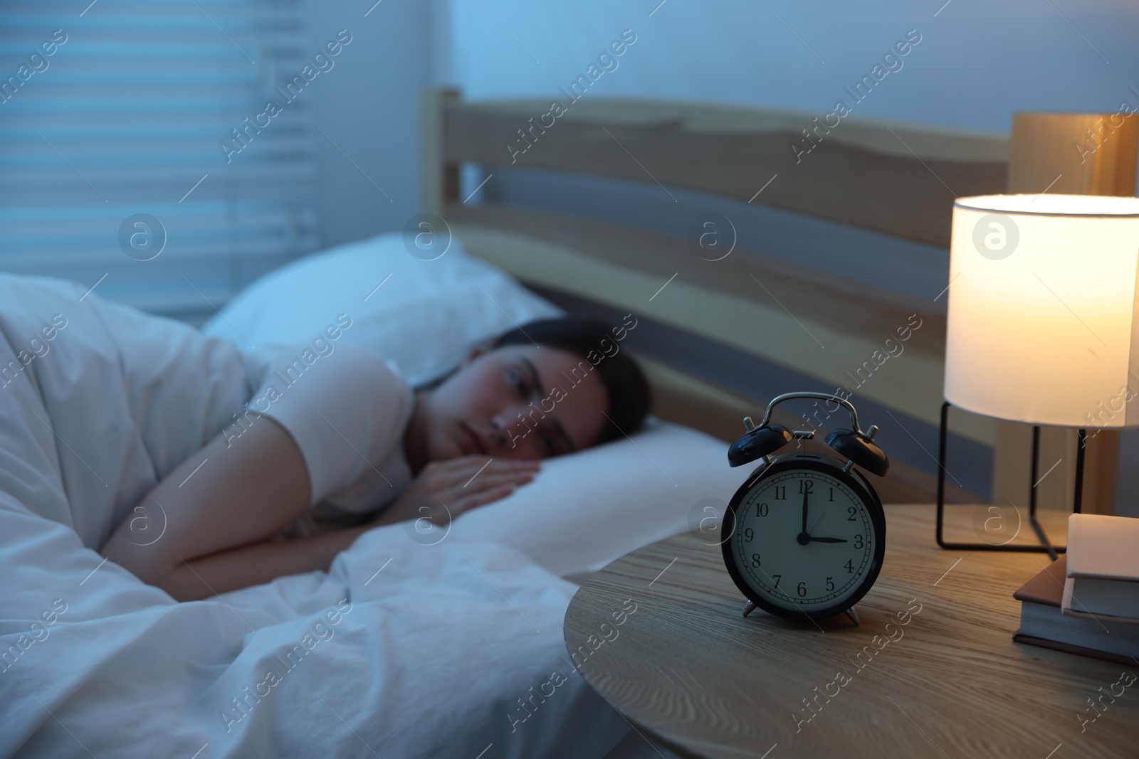 Frustrated young woman suffering from insomnia on bed indoors, focus on alarm clock Photo of Frustrated young woman suffering from insomnia on bed indoors, focus on alarm clock