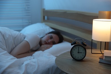 Photo of Frustrated young woman suffering from insomnia on bed indoors, focus on alarm clock