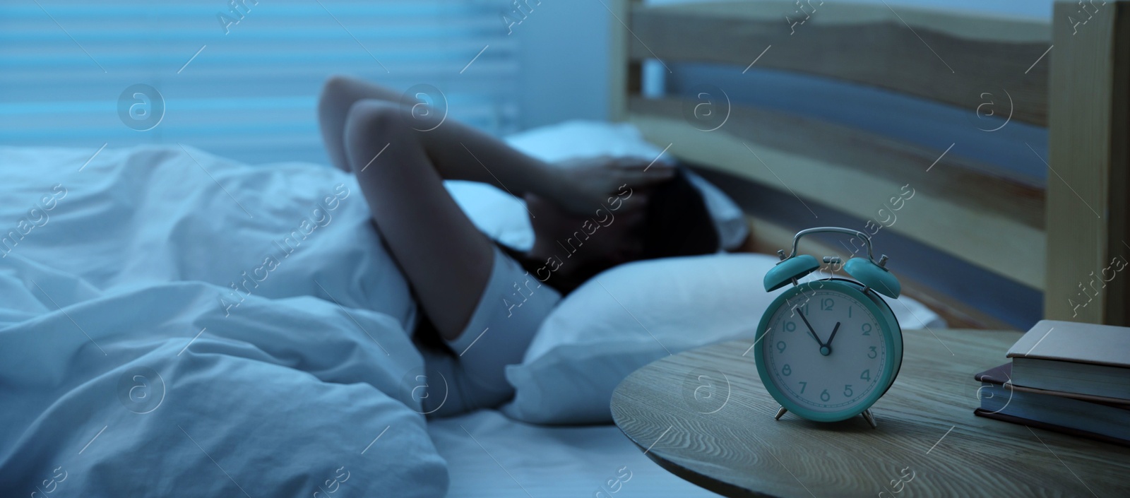 Frustrated young woman suffering from insomnia on bed indoors, focus on alarm clock Photo of Frustrated young woman suffering from insomnia on bed indoors, focus on alarm clock