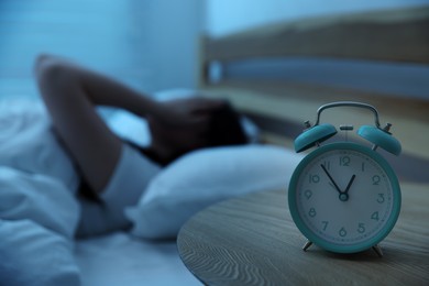 Photo of Frustrated young woman suffering from insomnia on bed indoors, focus on alarm clock