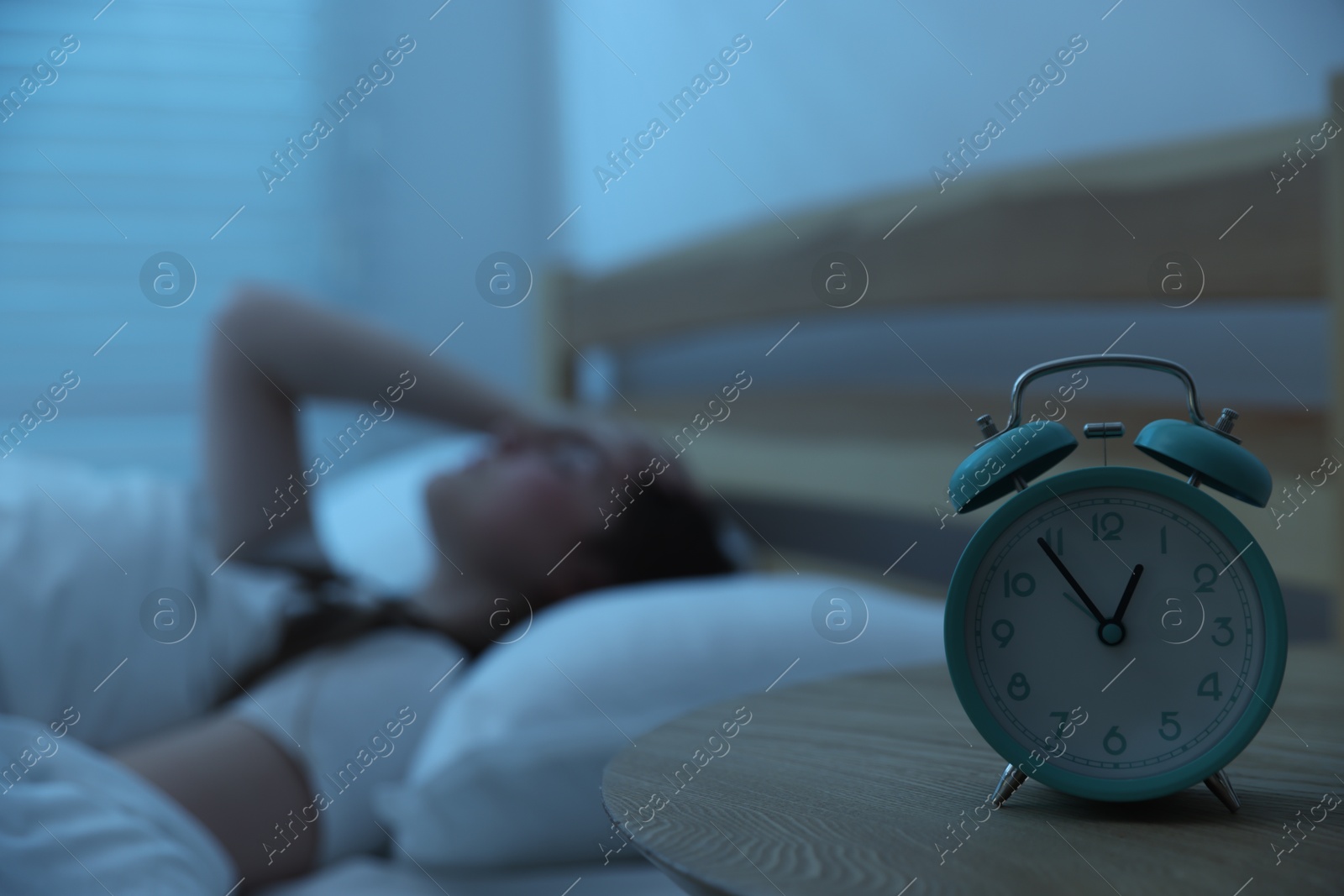 Frustrated young woman suffering from insomnia on bed indoors, focus on alarm clock Photo of Frustrated young woman suffering from insomnia on bed indoors, focus on alarm clock