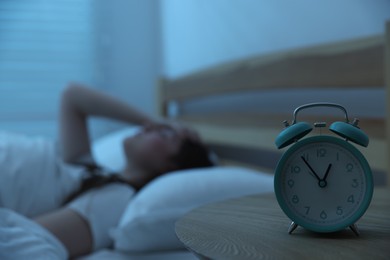 Photo of Frustrated young woman suffering from insomnia on bed indoors, focus on alarm clock