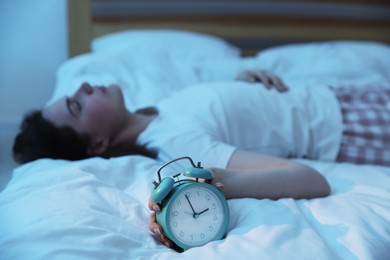 Photo of Frustrated young woman with alarm clock suffering from insomnia on bed indoors, selective focus
