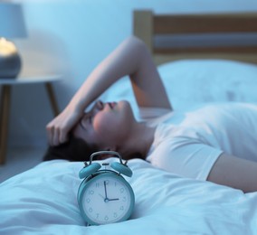 Photo of Frustrated young woman suffering from insomnia on bed indoors, focus on alarm clock