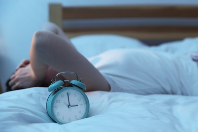 Photo of Frustrated young woman suffering from insomnia on bed indoors, focus on alarm clock