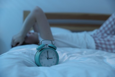 Photo of Frustrated young woman suffering from insomnia on bed indoors, focus on alarm clock