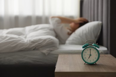 Photo of Upset young woman on bed at home, focus on alarm clock