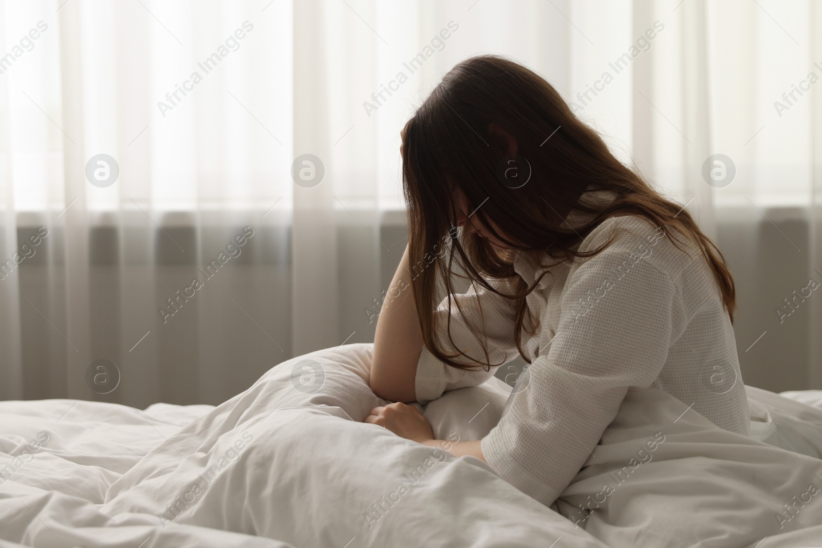 Upset young woman sitting on bed at home Photo of Upset young woman sitting on bed at home