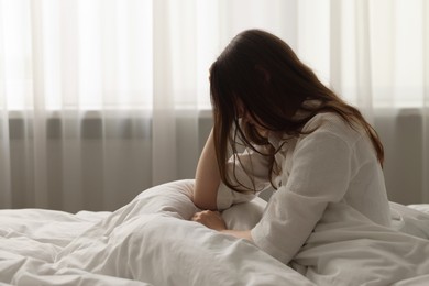 Photo of Upset young woman sitting on bed at home