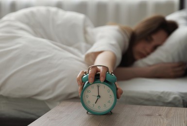 Photo of Upset young woman turning off alarm clock at home, selective focus
