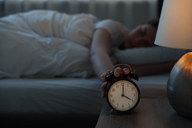 Photo of Frustrated young woman suffering from insomnia on bed indoors, focus on alarm clock
