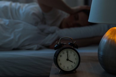 Photo of Frustrated young woman suffering from insomnia on bed indoors, focus on alarm clock