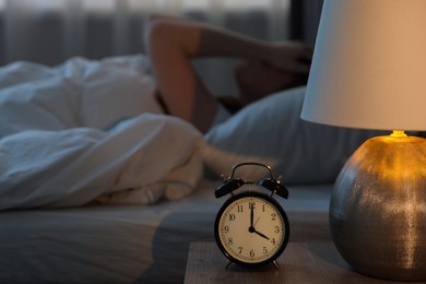 Photo of Frustrated young woman suffering from insomnia on bed indoors, focus on alarm clock