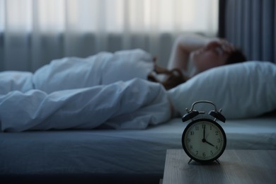 Photo of Frustrated young woman suffering from insomnia on bed indoors, focus on alarm clock
