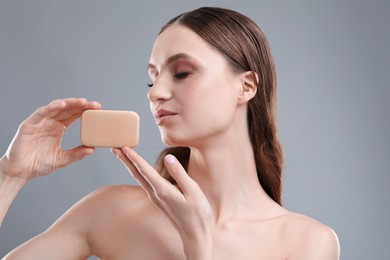 Photo of Beautiful woman with soap bar on grey background, closeup