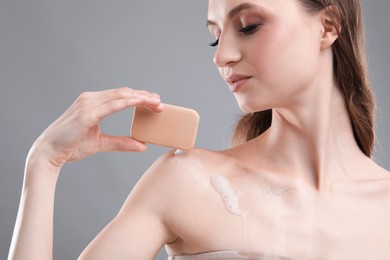 Photo of Beautiful woman with soap bar on grey background, closeup