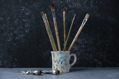 Photo of Brushes in cup and color paints on grey table
