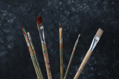 Photo of Many dirty paintbrushes on black background, closeup
