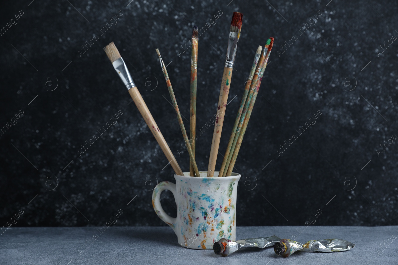 Brushes in cup and color paints on grey table Photo of Brushes in cup and color paints on grey table