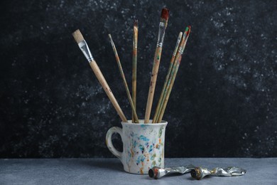 Photo of Brushes in cup and color paints on grey table