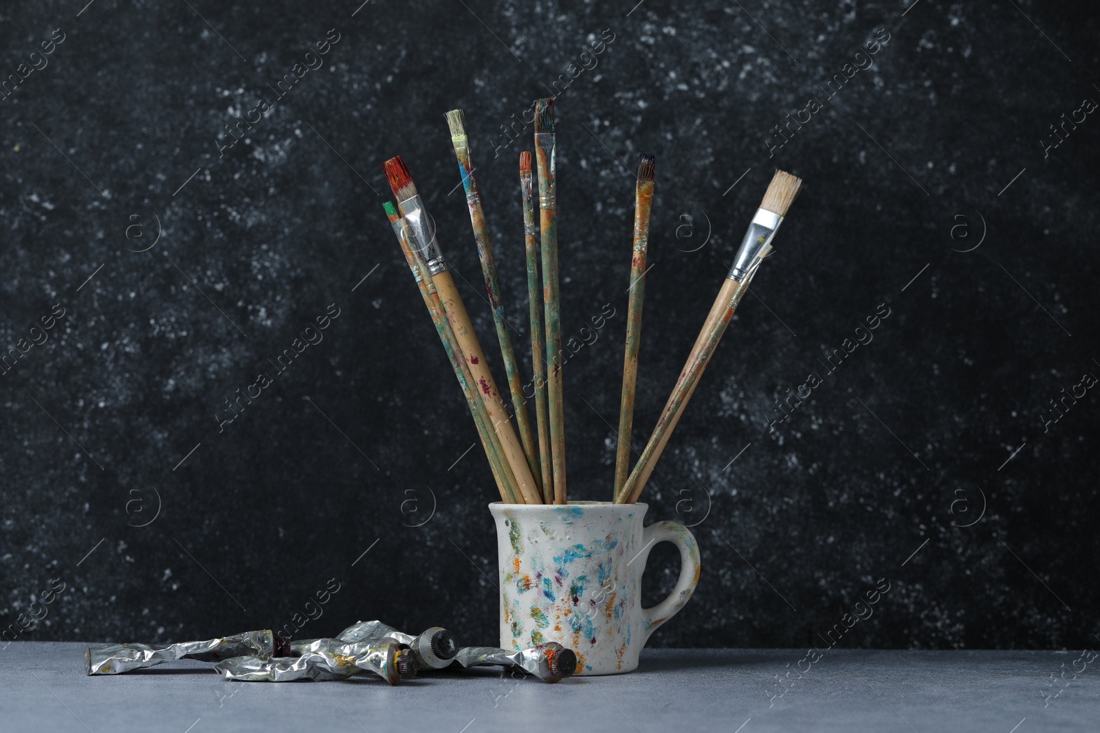 Brushes in cup and color paints on grey table Photo of Brushes in cup and color paints on grey table