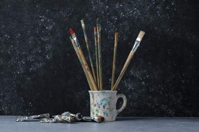 Photo of Brushes in cup and color paints on grey table