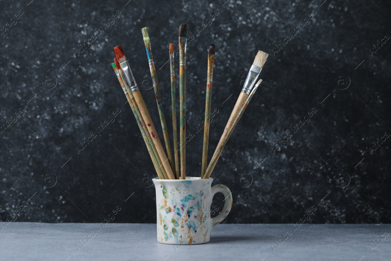 Dirty paintbrushes in cup on grey table Photo of Dirty paintbrushes in cup on grey table