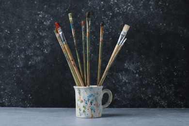 Photo of Dirty paintbrushes in cup on grey table