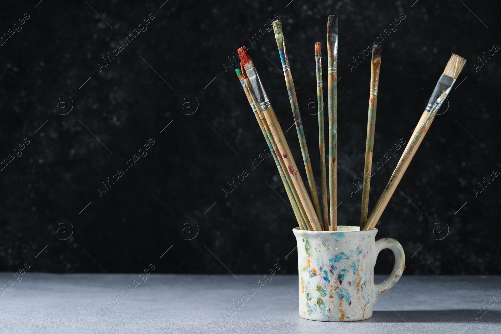 Dirty paintbrushes in cup on grey table. Space for text Photo of Dirty paintbrushes in cup on grey table. Space for text