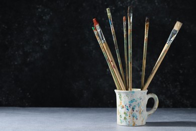 Photo of Dirty paintbrushes in cup on grey table. Space for text