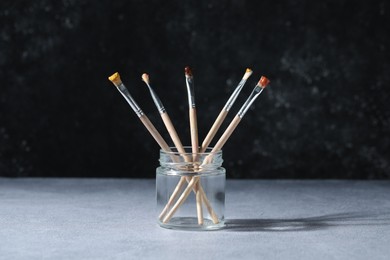 Photo of Brushes with color paints in jar on grey table