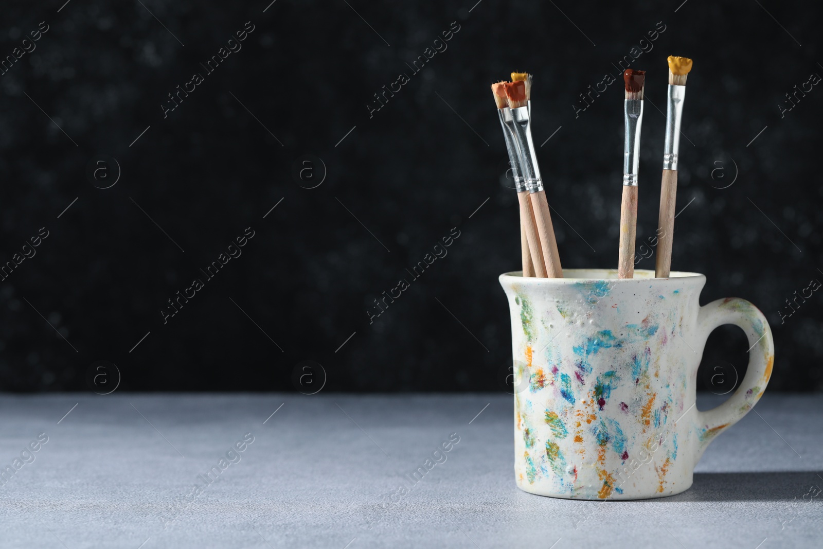 Brush with color paints in cup on grey table. Space for text Photo of Brush with color paints in cup on grey table. Space for text