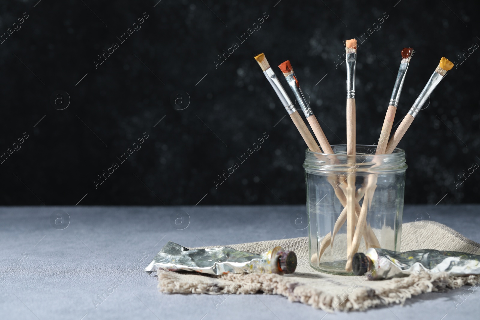 Brushes in jar and color paints on grey table. Space for text Photo of Brushes in jar and color paints on grey table. Space for text