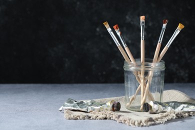 Photo of Brushes in jar and color paints on grey table. Space for text