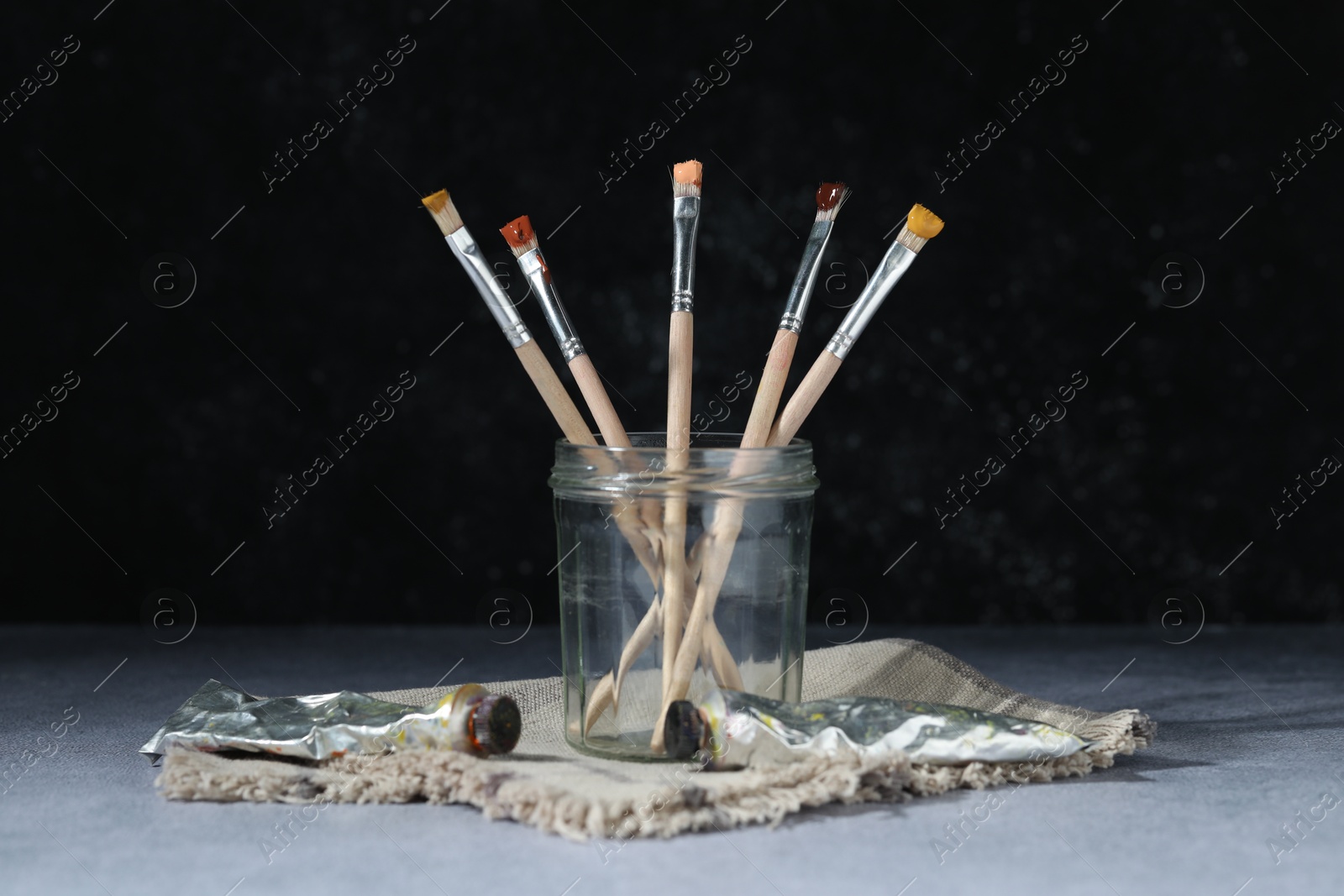 Brushes in jar and color paints on grey table Photo of Brushes in jar and color paints on grey table