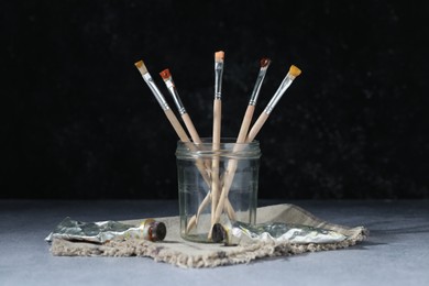 Photo of Brushes in jar and color paints on grey table