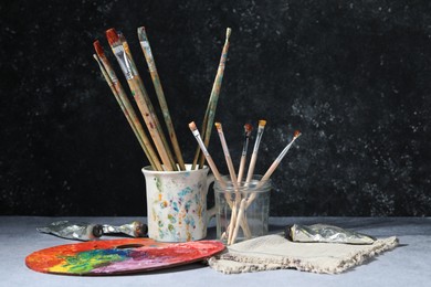 Photo of Brushes, palette and color paints on grey table