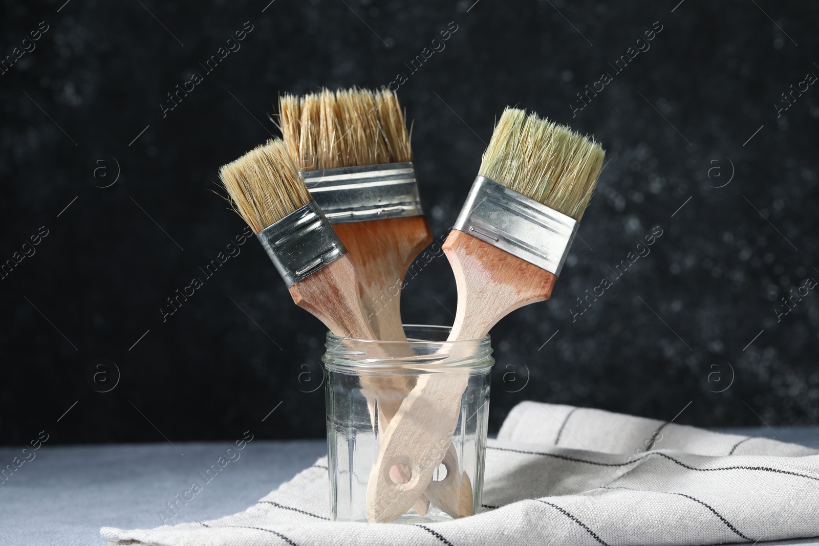 Three paintbrushes in jar on grey table Photo of Three paintbrushes in jar on grey table