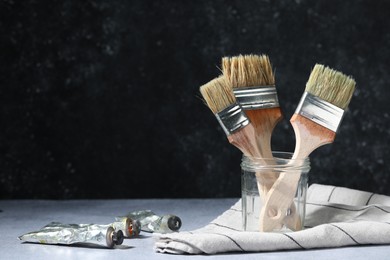 Photo of Brushes in jar and color paints on grey table. Space for text