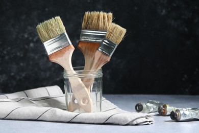Photo of Brushes in jar and color paints on grey table