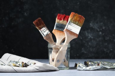Photo of Brushes in jar and color paints on grey table