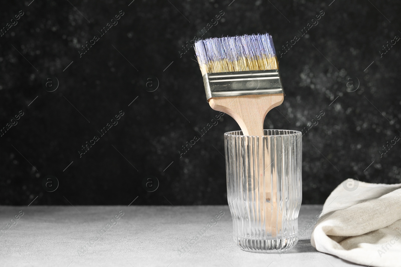 Brush with color paints in glass on grey table. Space for text Photo of Brush with color paints in glass on grey table. Space for text