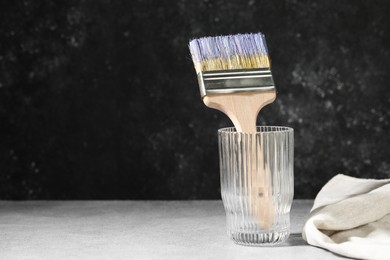 Photo of Brush with color paints in glass on grey table. Space for text