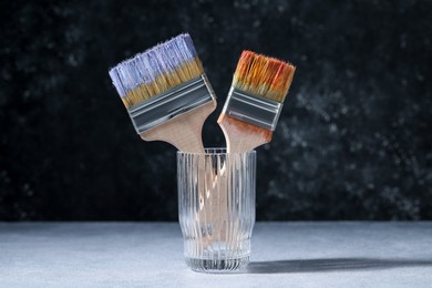 Photo of Brushes with color paints in glass on grey table