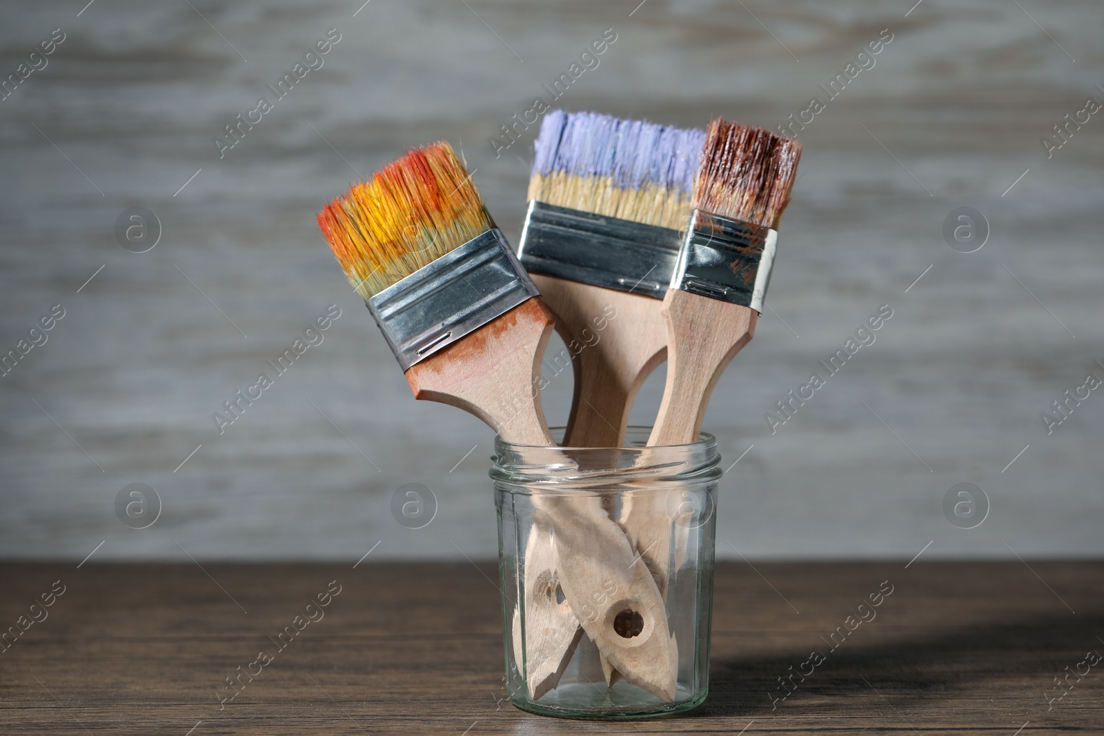 Brush with color paints in jar on wooden table Photo of Brush with color paints in jar on wooden table
