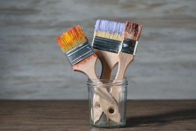 Photo of Brush with color paints in jar on wooden table